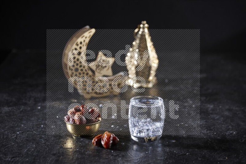 تمر في وعاء معدني مع الماء بجانب فوانيس ذهبية علي خلفية سوداء