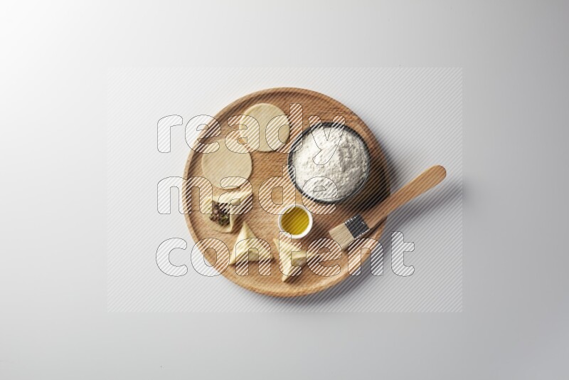 two closed sambosas and one open sambosa filled with meat while flour, and oil with oil brush aside in a wooden dish on a white background