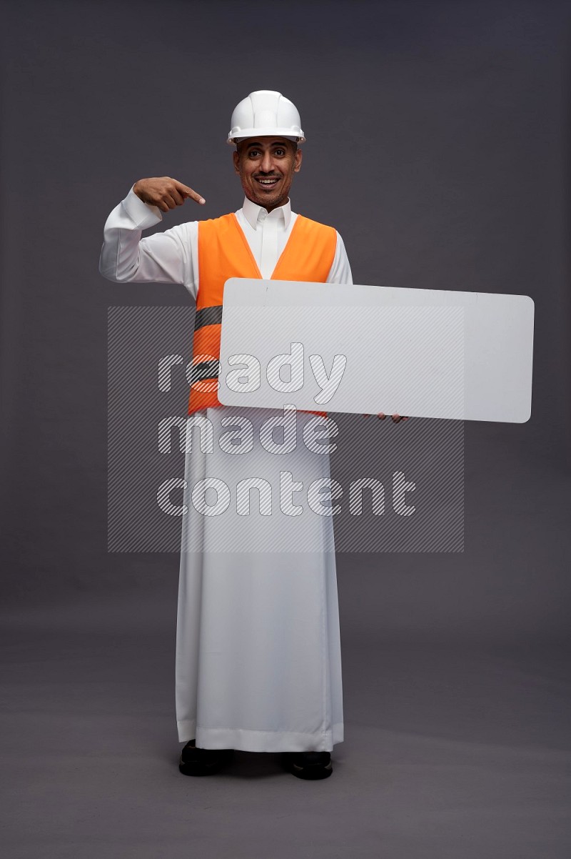 Saudi man wearing thob with engineer vest standing holding board on gray background