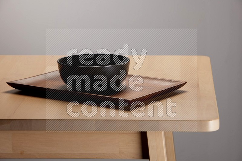 black bowl placed on a rectangular wooden tray on the edge of wooden table