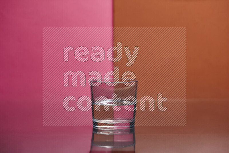 The image features a clear glassware filled with water, set against pink and dark orange background