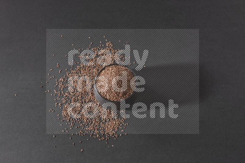 وعاء فخاري أسود ممتلئ بحبوب بذر الكتان محاط بالبذور على أرضية سوداء