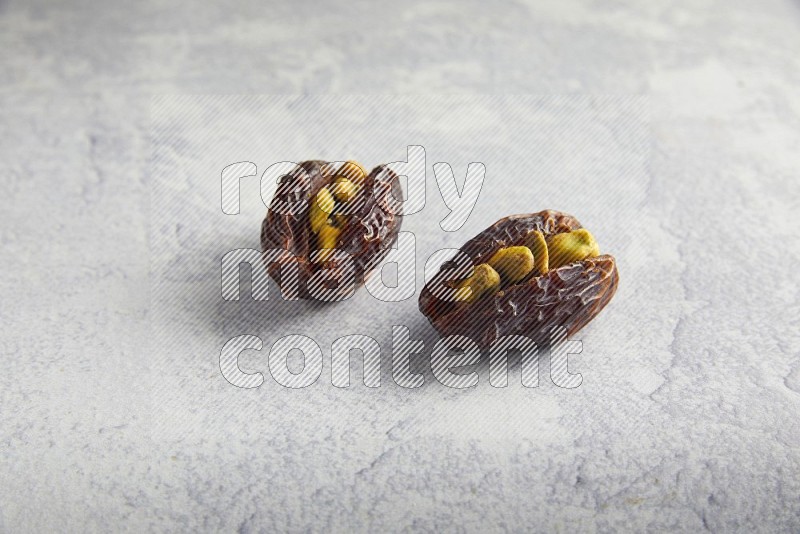 two pistachio stuffed madjoul date on a light grey background