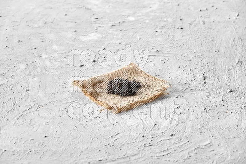 Black pepper on burlap fabric on a textured white flooring