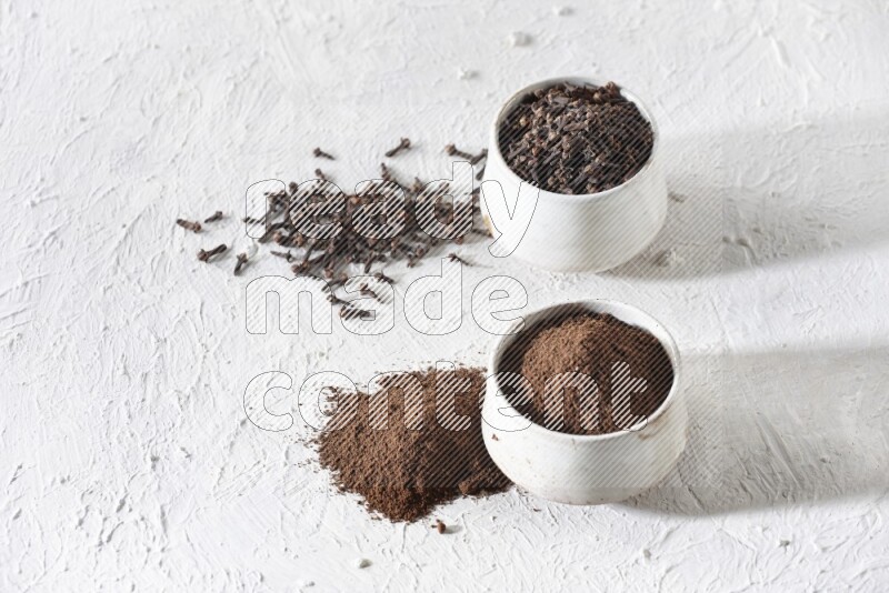 2 Beige ceramic bowls, one full of cloves and the other full of powder on textured white flooring