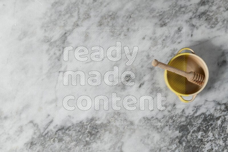 Multicolored pottery bowl with wooden honey dipper in it on grey marble background