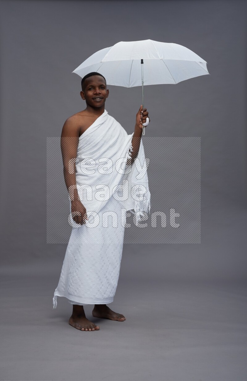 A man wearing Ehram Standing holding umbrella on gray background