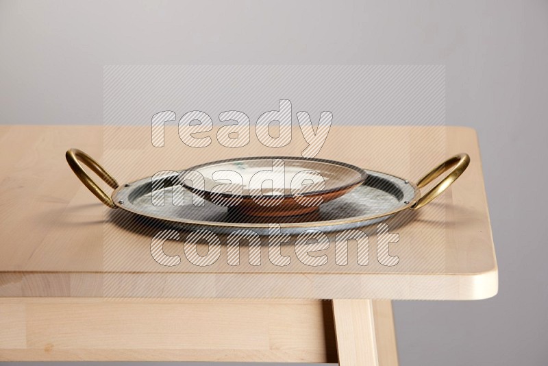 multicolored plate placed on a rounded stainless steel tray with golden handels on the edge of wooden table