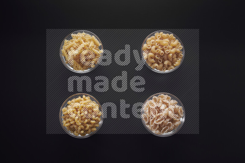 Different pasta types in glass bowls on black background