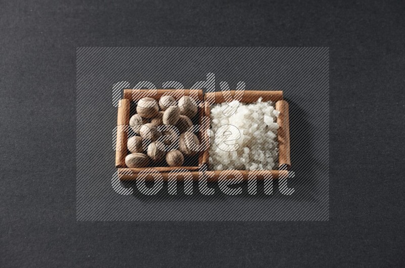 مربعان من أعواد القرفة ممتلئان بجوزة الطيب والملح الأبيض علي خلفية سوداء