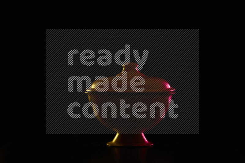 A vintage metal pot with colored rim light against black background