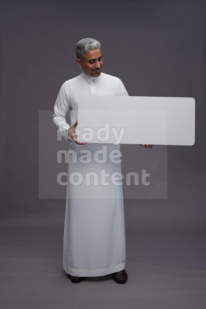 Saudi man wearing thob standing holding board on gray background