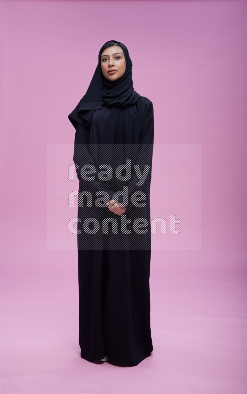 Saudi woman wearing Abaya standing interacting with the camera on pink background