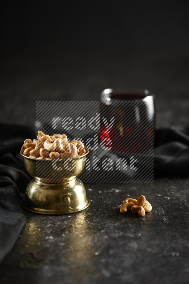 Nuts in a metal bowl with hibiscus and a napkin in a dark setup