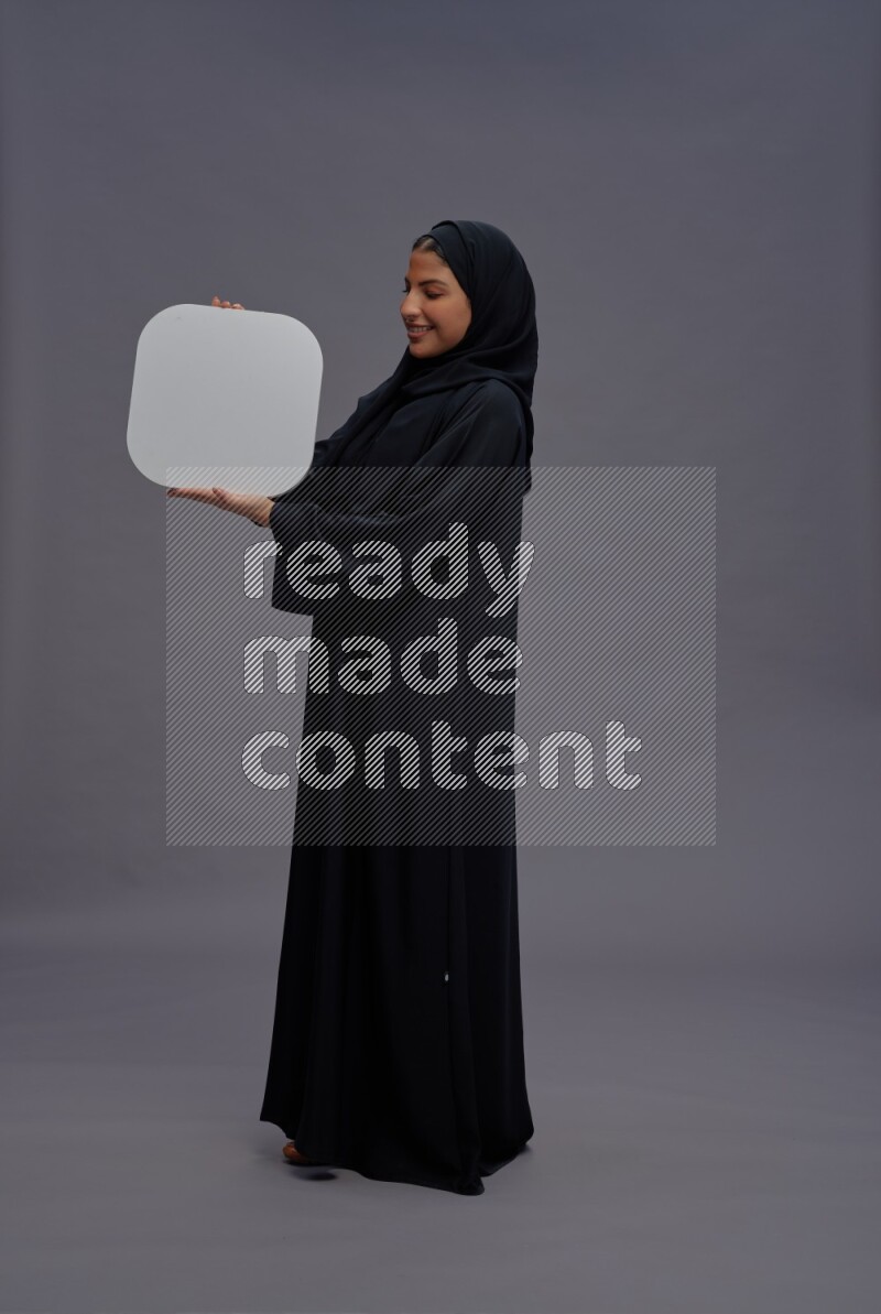 Saudi woman wearing Abaya standing holding social media sign on gray background