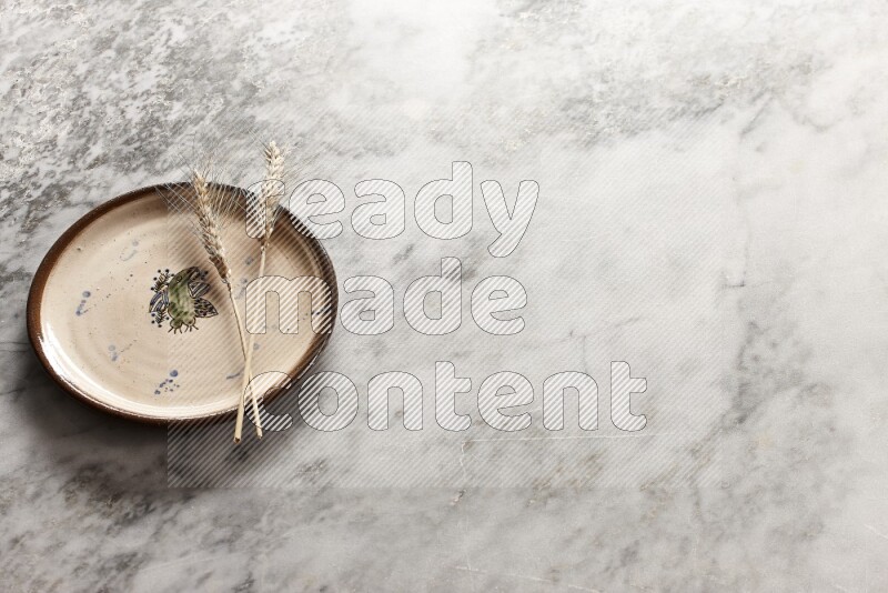 Wheat stalks on decorative pottery plate on grey marble background