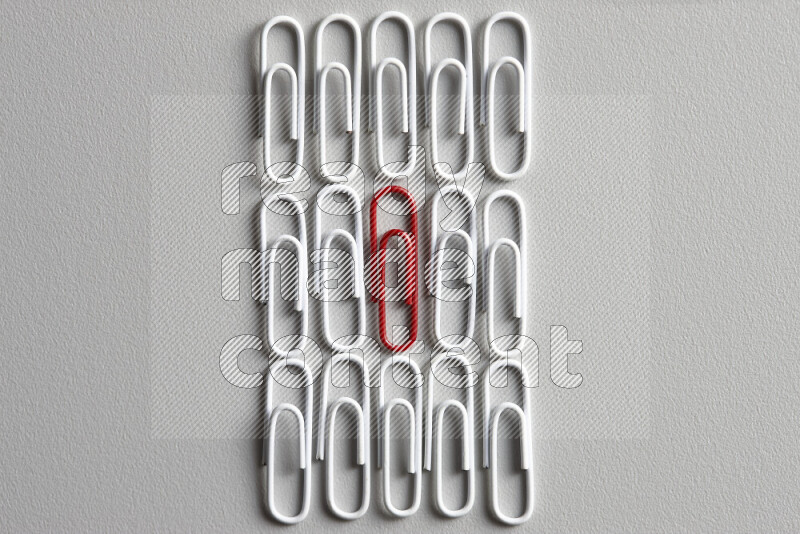 A red paperclip surrounded by bunch of white paperclips on grey background