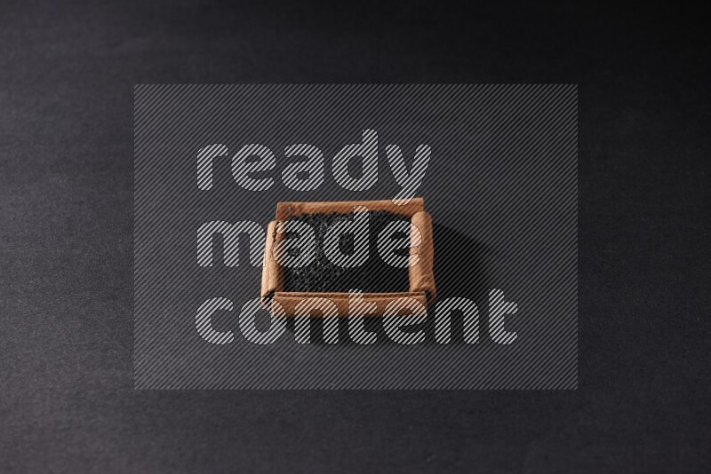 أربعة من أعواد القرفة مكونة شكل مربع بداخلها حبة البركة علي خلفية سوداء