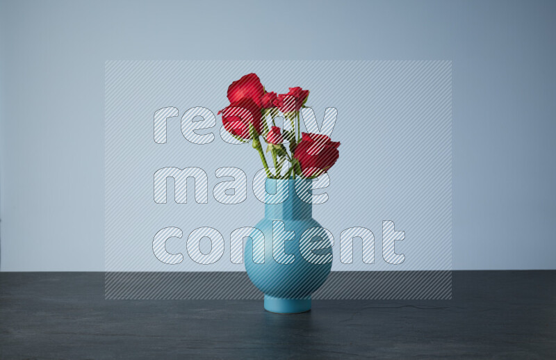 An arrangement of vivid red roses in a blue vase on black marble background