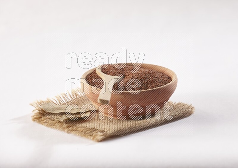 A wooden bowl and spoon full of garden cress seeds on burlap fabric on a white flooring
