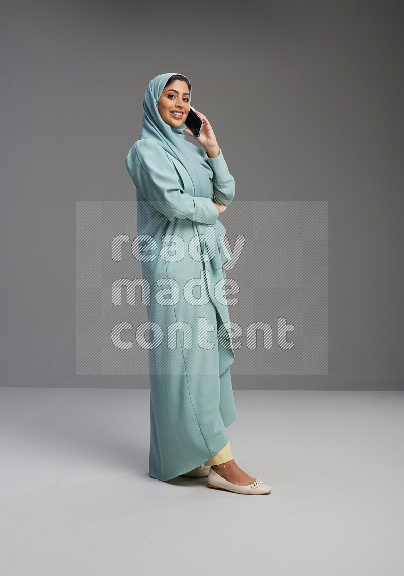 Saudi Woman wearing Abaya standing talking on phone on Gray background