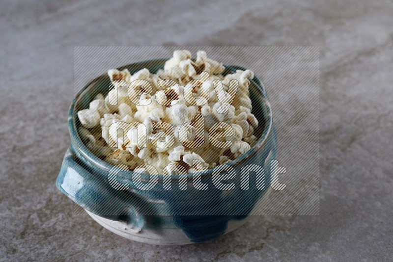 popcorn in a multi-colored handheld ceramic bowl on a grey textured countertop