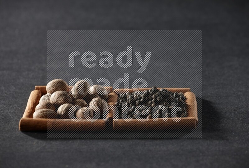 مربعان من أعواد القرفة ممتلئان بجوزة الطيب وحبوب الفلفل الأسود علي خلفية سوداء