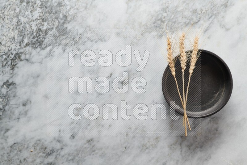 Wheat stalks on black pottery oven plate on grey marble background