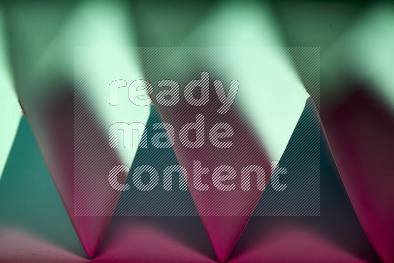 A close-up abstract image showing sharp geometric paper folds in green and pink gradients