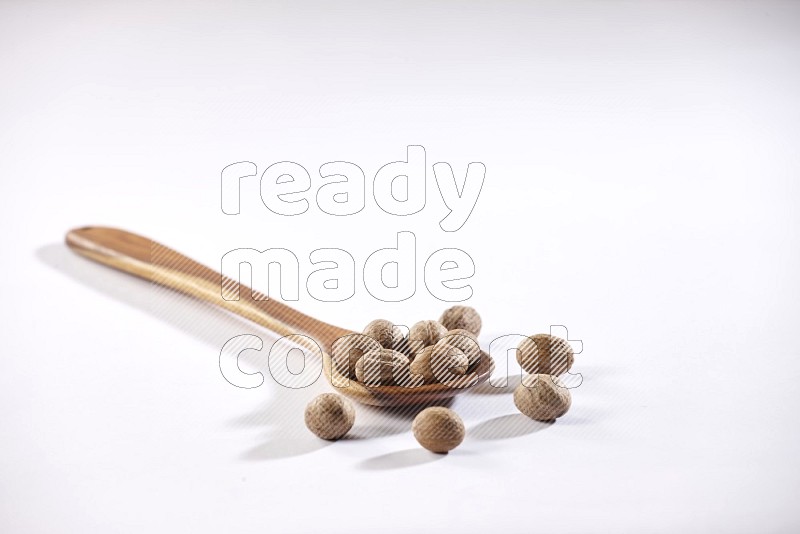 A wooden ladle full of whole nutmeg seeds on a white flooring