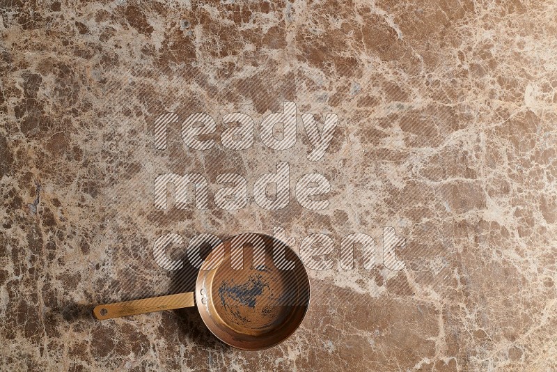 Top View Shot Of A Small Copper pan On beige Marble Flooring