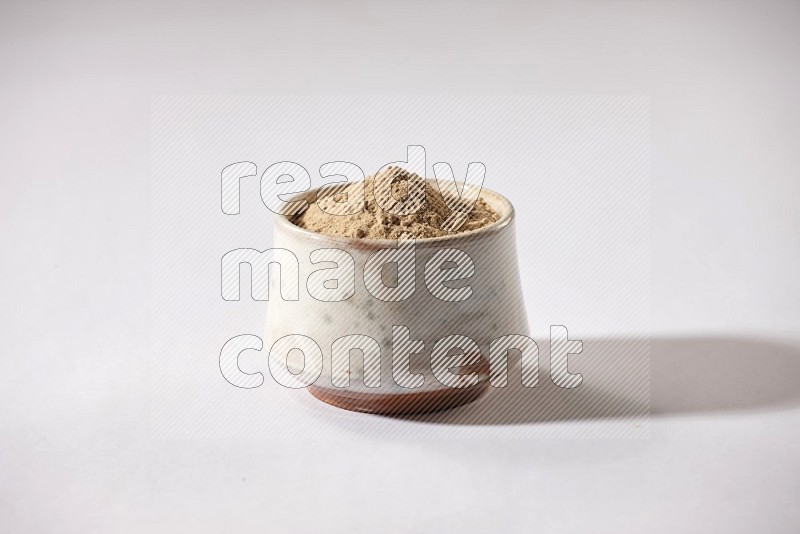 A beige pottery bowl full of garlic powder on a white flooring in different angles