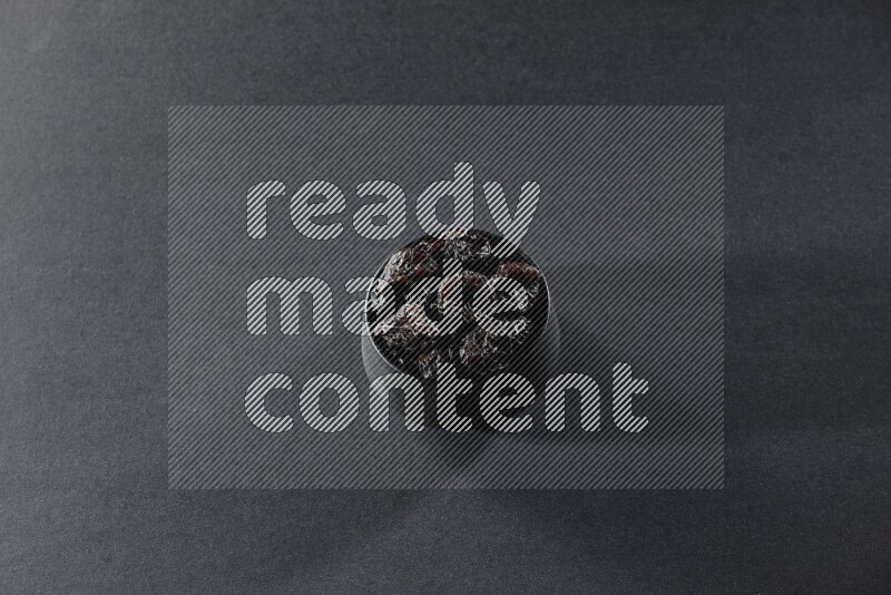 وعاء فخاري أسود ممتلئ بالبرقوق المجفف على خلفية سوداء