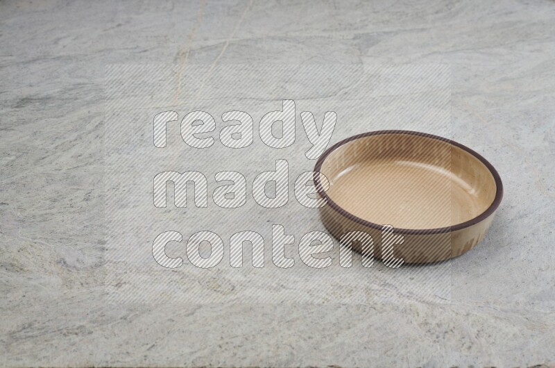 A beige pottery oven bowl on grey marble background