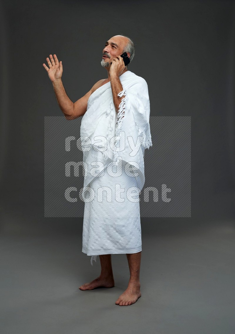 A man wearing Ehram Standing talking on phone on gray background