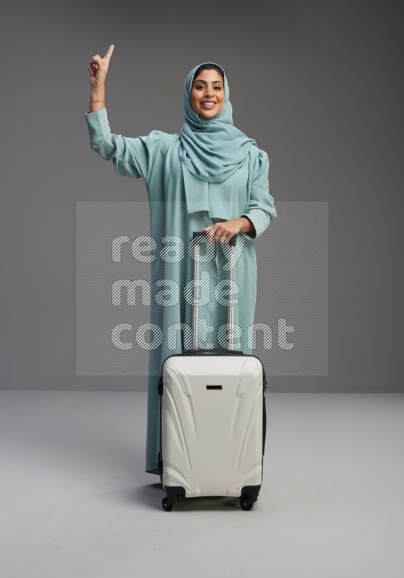 Saudi Woman wearing Abaya standing holding Travel bag on Gray background