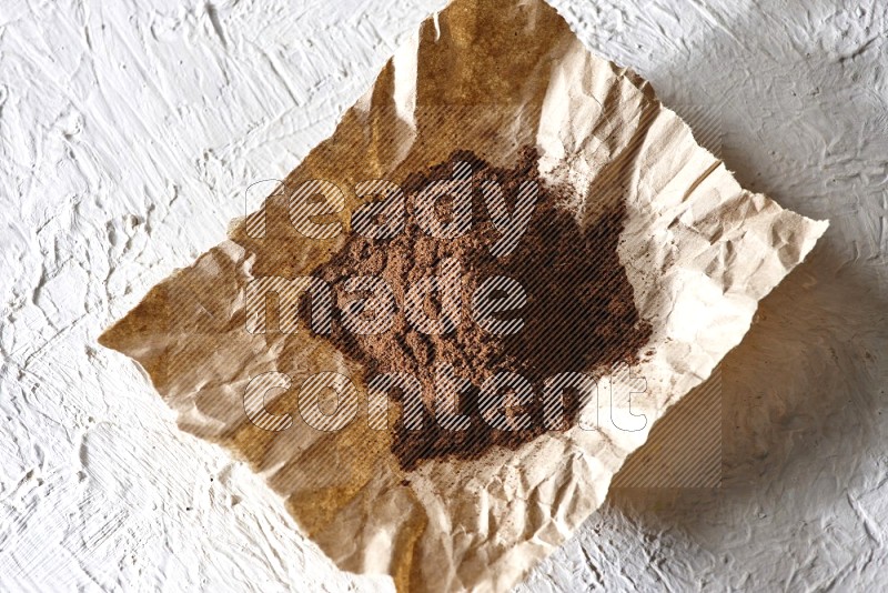 Cloves powder on crumpled piece of paper on a textured white flooring