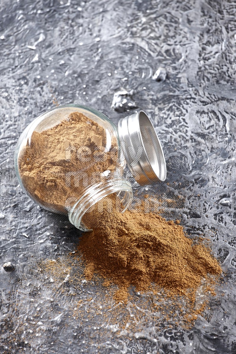 Flipped herbal glass jar full of cinnamon powder on textured black background