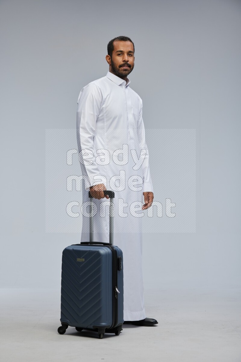 Saudi man wearing thob standing holding Travel bag on Gray background
