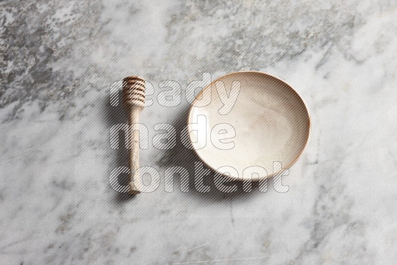 Beige pottery plate with wooden honey dipper on the side on grey marble background