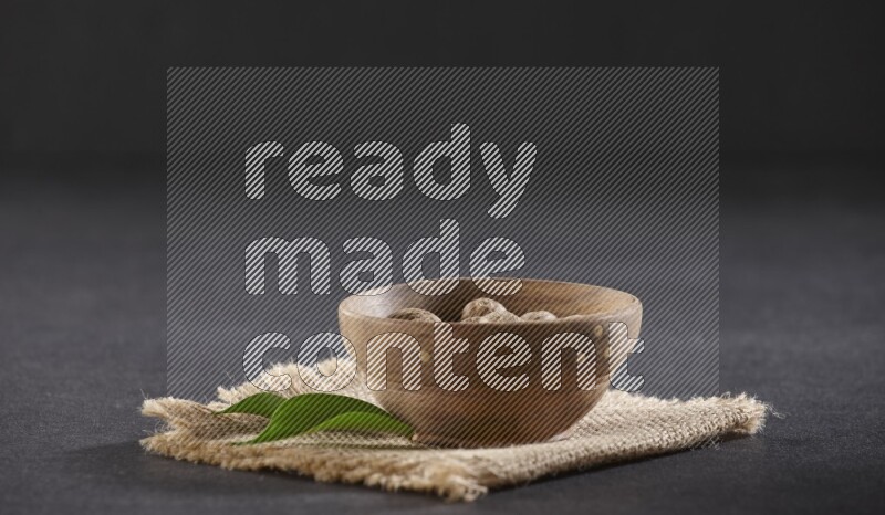 وعاء خشبي ممتلئ بحبوب جوزة الطيب الكاملة موضوع علي قطعة من قماش الخيش علي خلفية سوداء