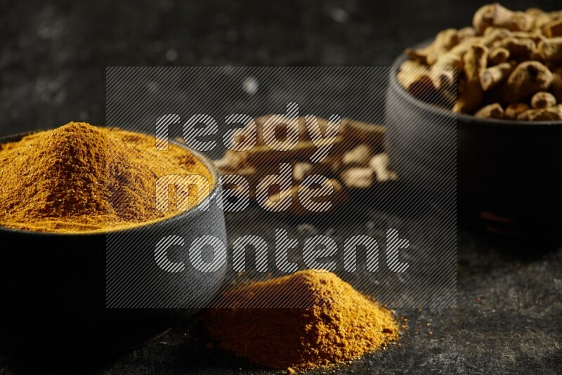 وعاءان من الفخار باللون الأسود، أحدهما ممتلئ ببودرة الكركم والآخر ممتلئ بأصابع كاملة من الكركم المجفف على خلفية سوداء