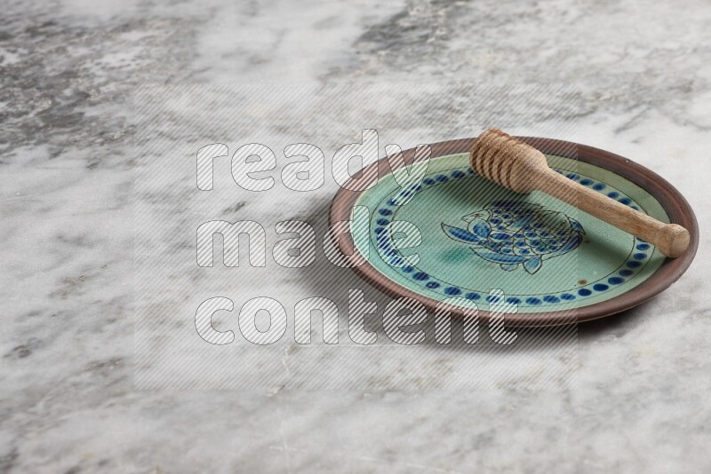 Decorative pottery plate with wooden honey dipper in it on grey marble background