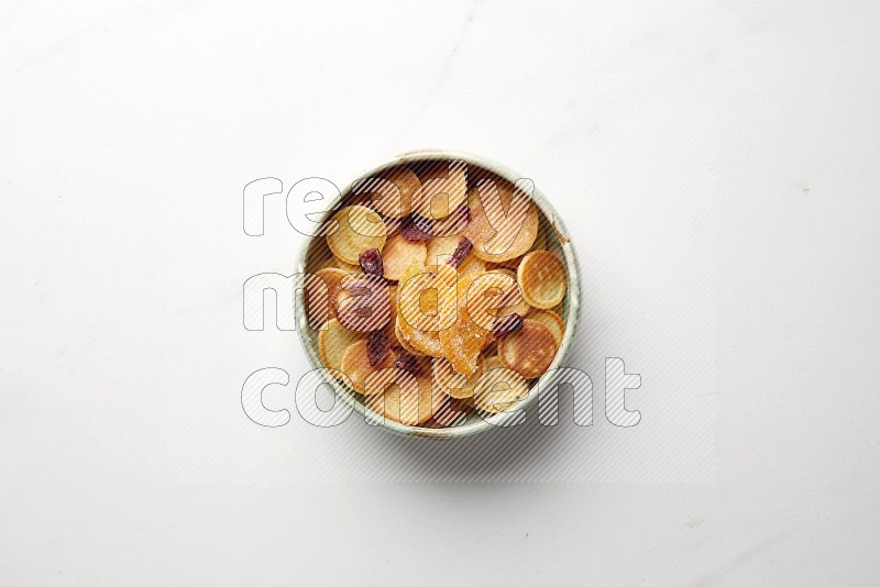 Top-view shot of orange candy cereal pancakes in a round bowl on white background