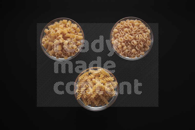 Different pasta types in glass bowls on black background