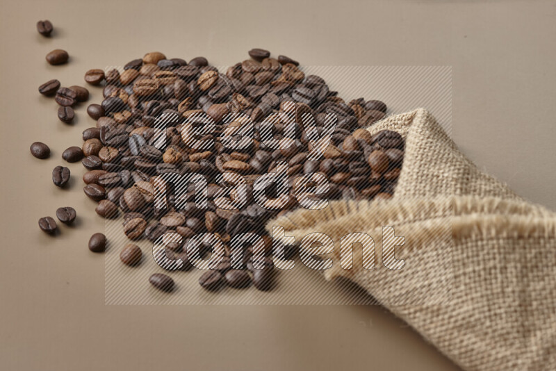 Spilled roasted coffee beans from its pack on beige background
