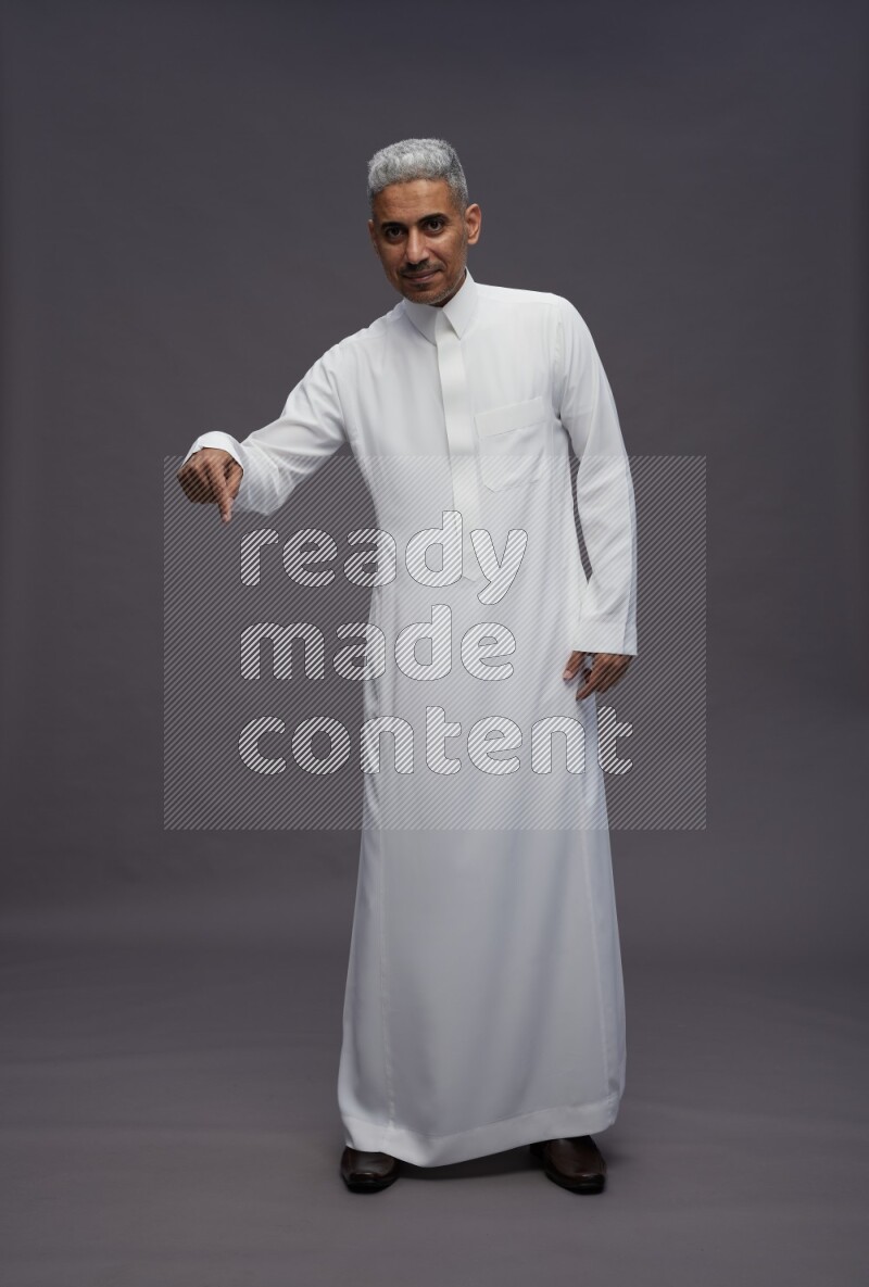 Saudi man wearing thob standing interacting with the camera on gray background