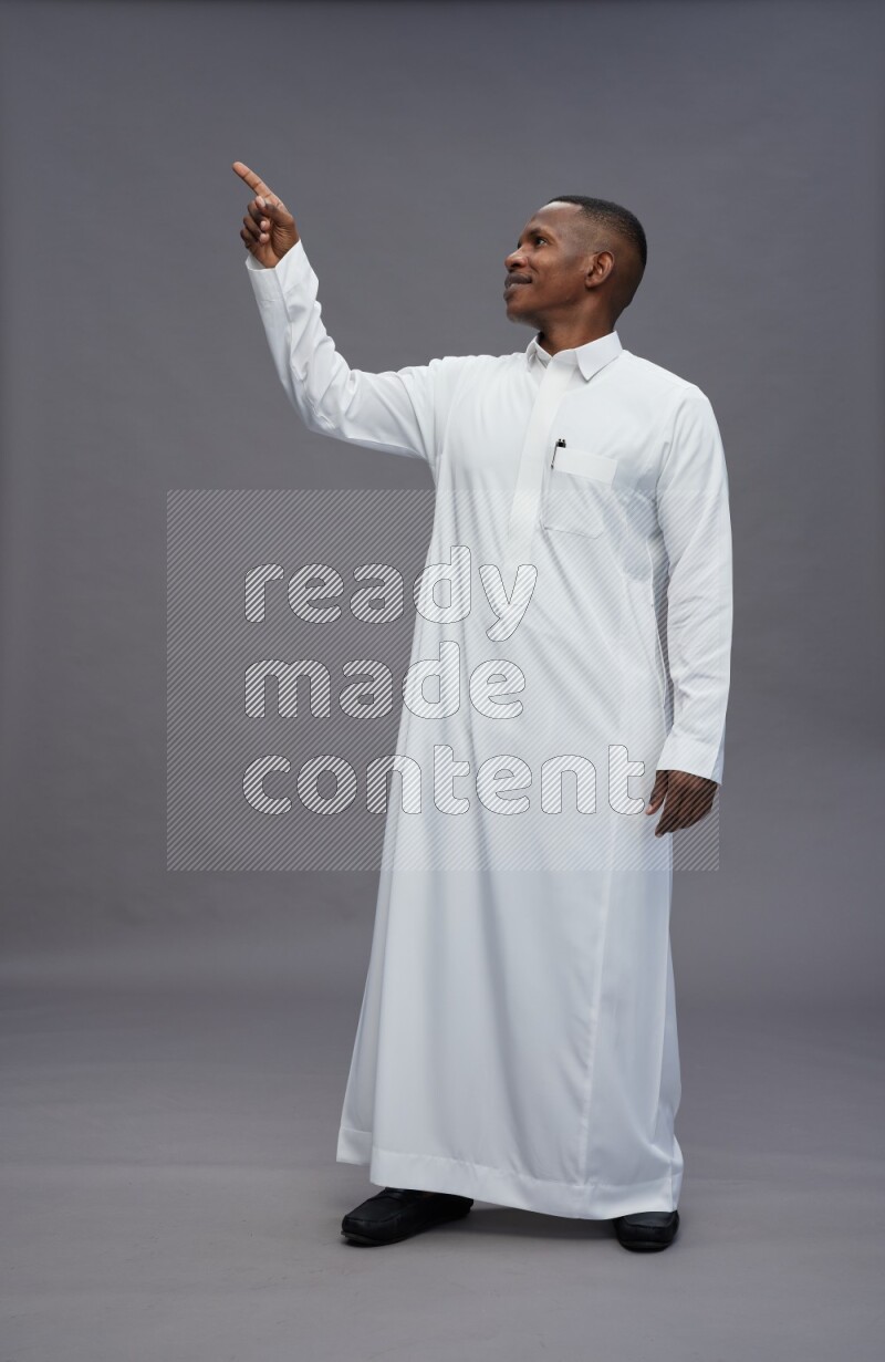 Saudi man wearing thob standing interacting with the camera on gray background