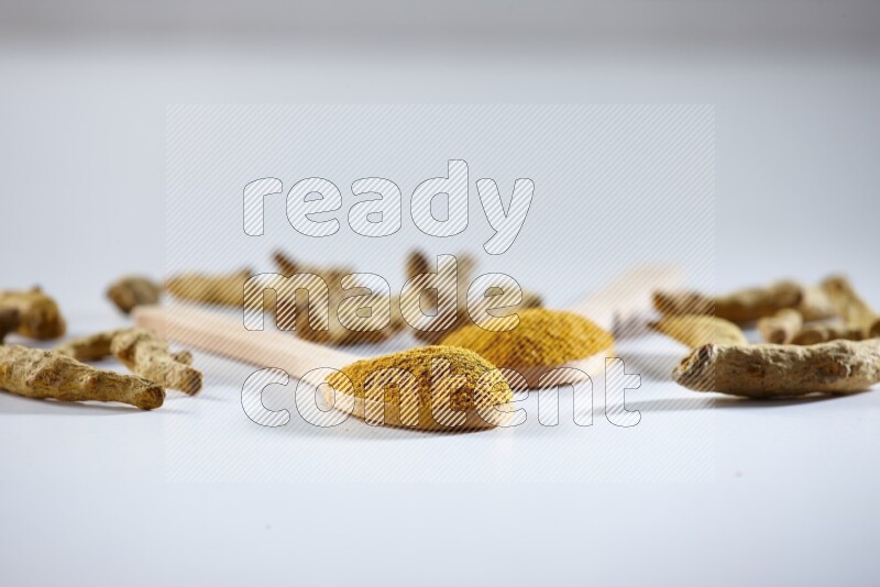 2 wooden spoons full of turmeric powder with dried turmeric fingers beside it on white flooring