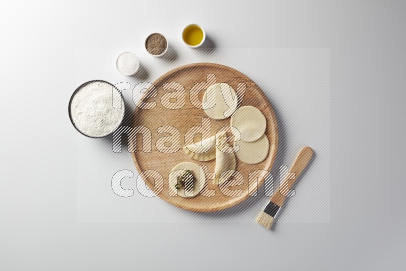 two closed sambosas and one open sambosa filled with meat while flour, salt, black pepper and oil with oil brush aside in a wooden dish on a white background